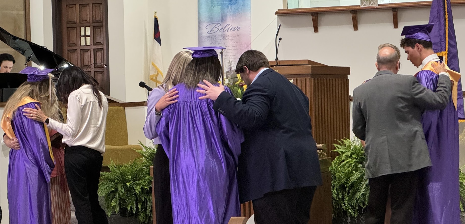 Teachers and administrators gather around seniors in prayer during Baccalaureate
